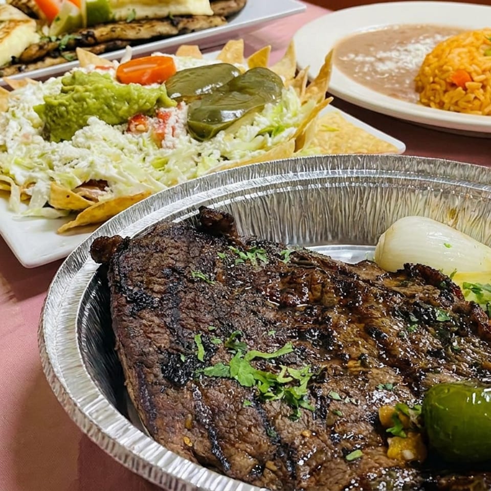 Grilled steak with roasted vegetables, nachos topped with guacamole, and Mexican rice arranged on a restaurant table.